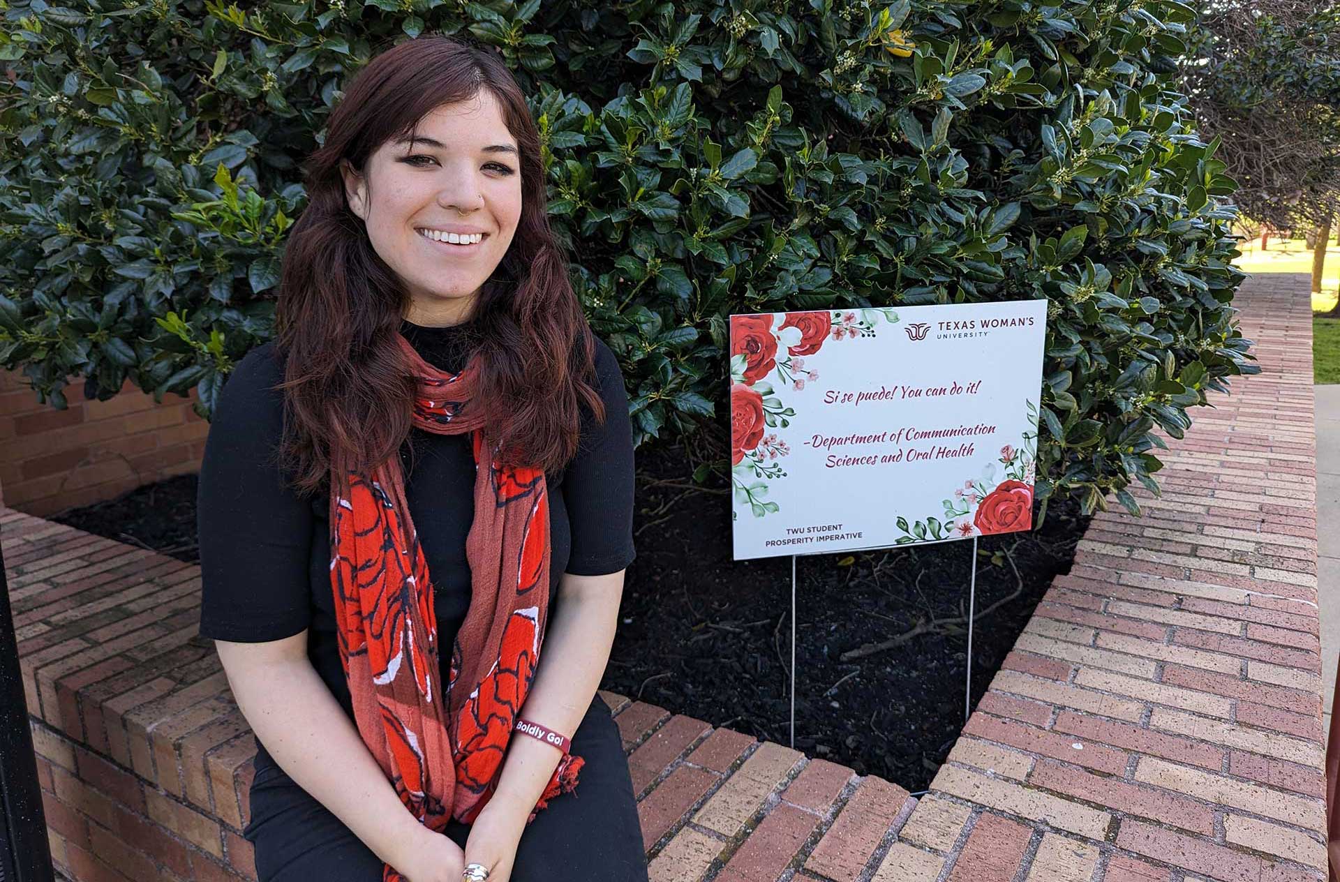 A TWU student sits next to a sign