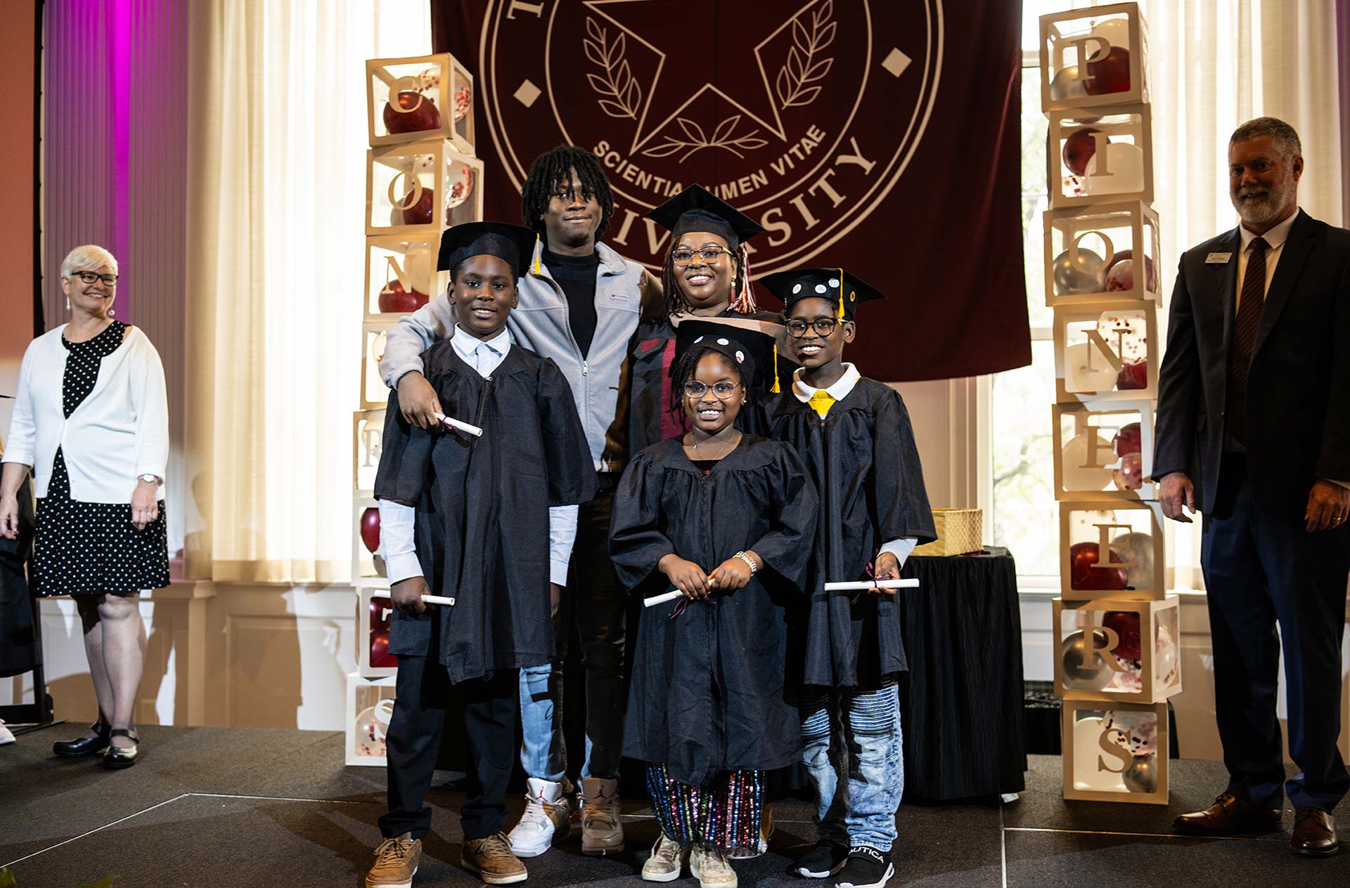 An entire family, both parents and children, wear graduation regalia and hold diplomas