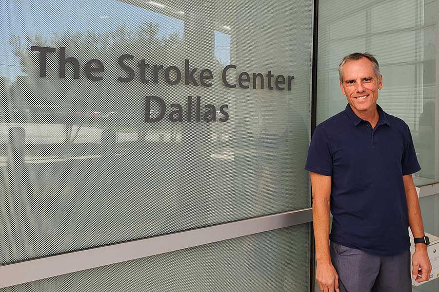 man stands in front of window with The Stroke Center - Dallas written on it 