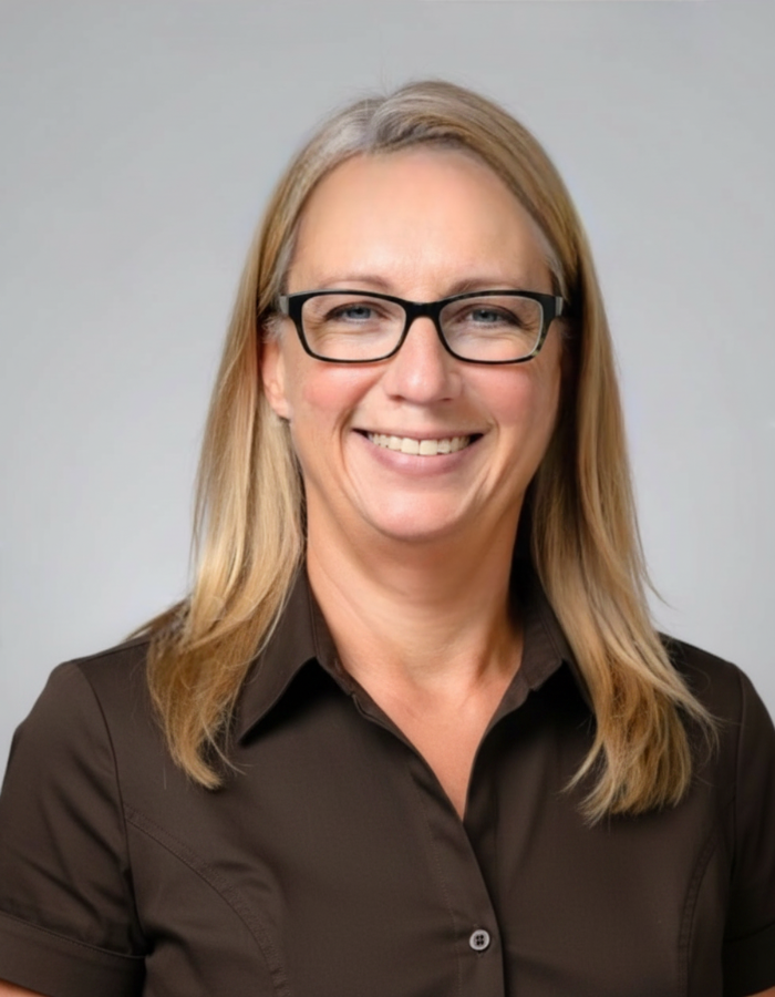 Professional headshot of Niki Peyton, smiling in front of a neutral background in business casual attire.