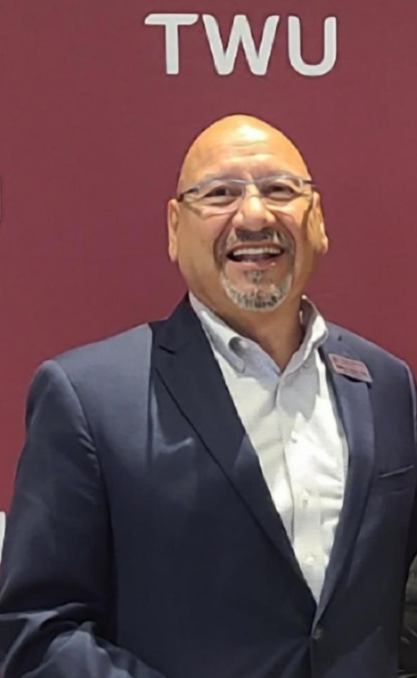 Professional headshot of Henry Torres wearing business attire, facing the camera with a dark marron colored TWU background