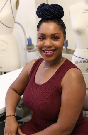 Jasmine Foster smiling in a studio setting with a dress form behind her.