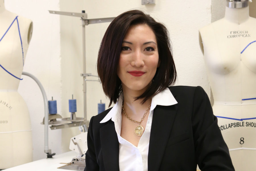 Kelsey Sager smiling while standing in a studio setting with dress forms behind her.