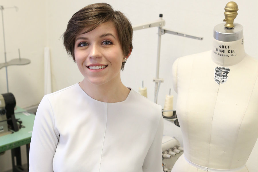 Lillia Dean smiling in a studio setting with a dress form behind her.