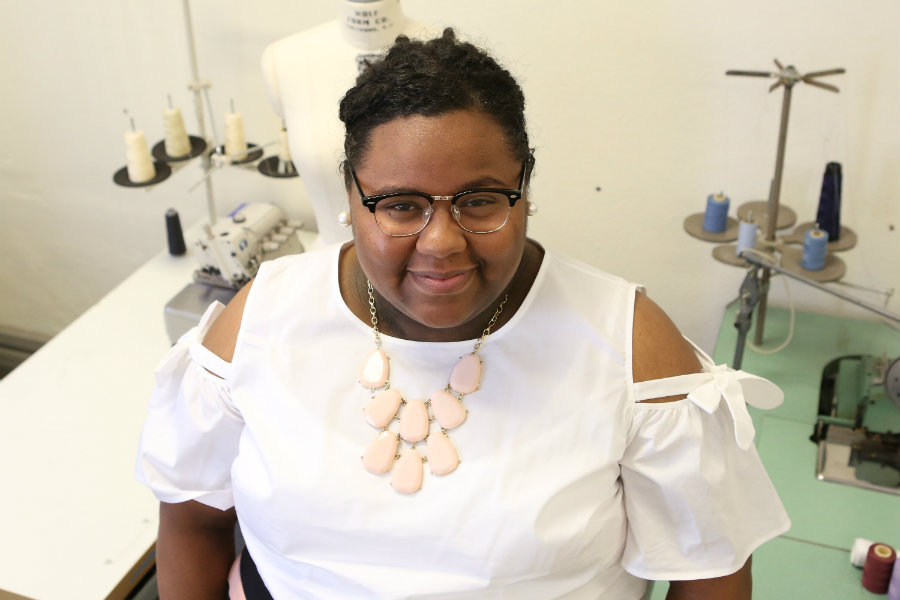 Ziaira Norman smiling in a studio setting with a dress form behind her.