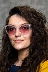 Portrait of Kristina Smith. Long wavy hair, wearing rose-tinted glasses