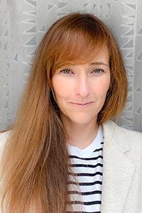Headshot of Meg Griffiths. Woman with reddish-brown hair, white and blue striped shirt, cream blazer