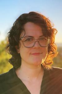 Headshot of Julie Libersat. Woman with dark brown curly, sun setting behind her