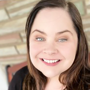 Natalie McCurley headshot - smiling white woman with blue eyes and brown hair, wearing a black top