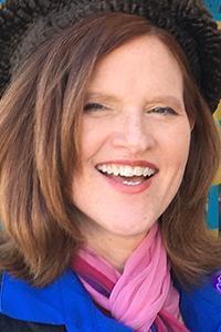 Headshot of Sheli Petersen. Woman with reddish-brown hair, smiling, wearing a hat and scarf