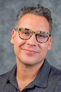 Portrait of Giovanni Valderas. Man with salt and pepper curly hair, wearing glasses, and dark polo